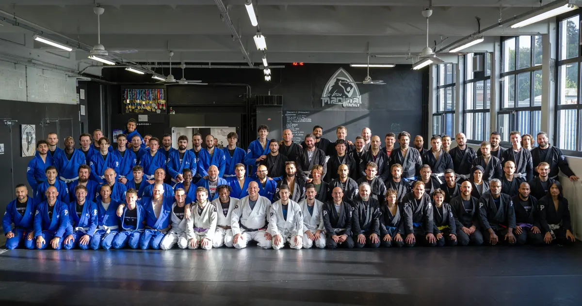 Les élèves de l'académie, en kimono bleu, blanc et noir, réunis sur les tapis devant le logo Manimal Family