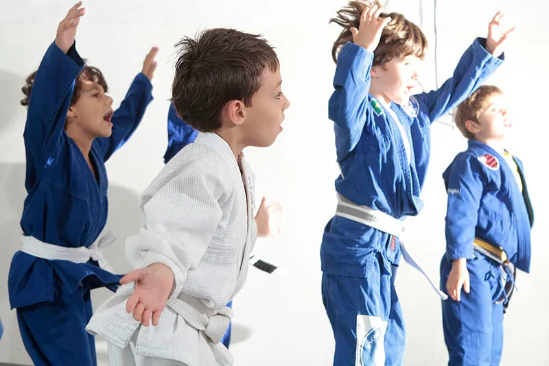 Quatre enfants en kimono bleu et blanc, bras levés, pendant un cours kids