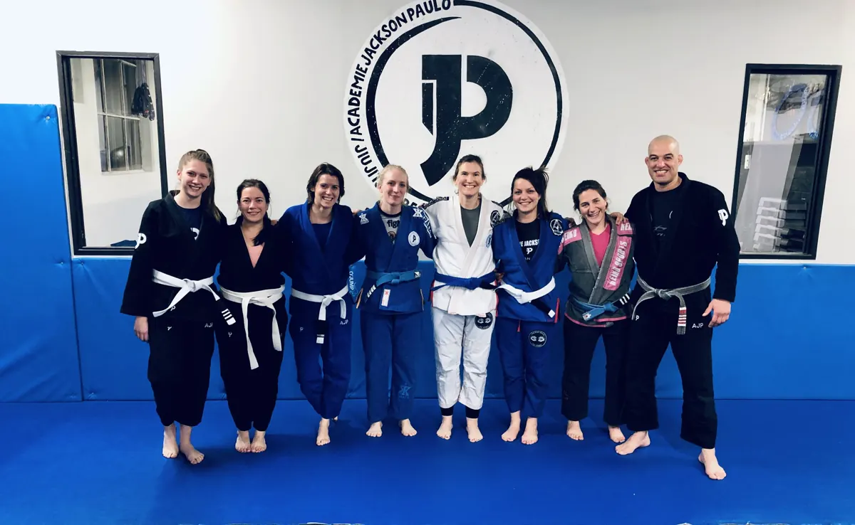 Les pratiquantes du cours ladies et leur professeur, en kimono, devant le logo de l'académie